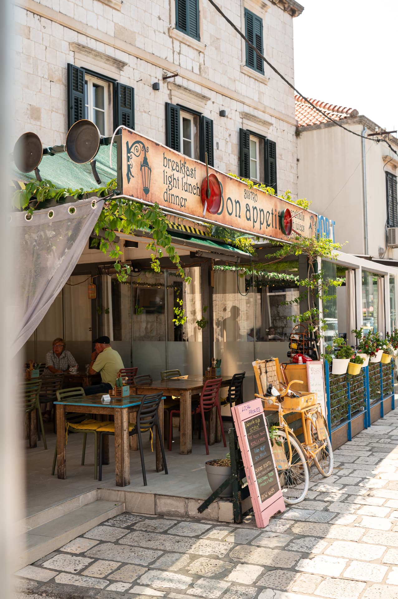 The Bon Appetit terrace in Gruž with mismatched painted tables, chairs and a yellow bicycle